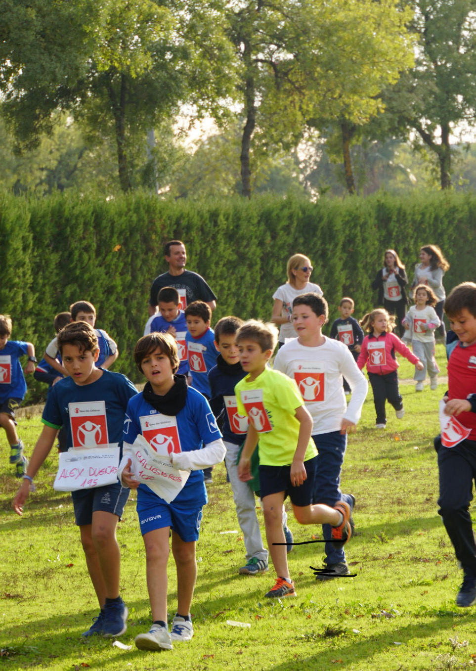 Alumnos corriendo por una zona de césped con dorsales de la carrera solidaria