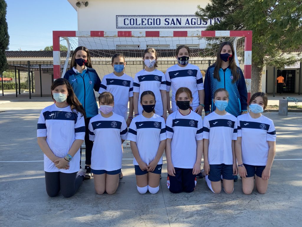 Equipo de voleibol posando con mascarilla ante una portería del patio