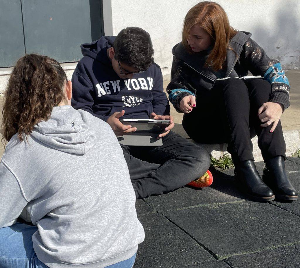 Tres alumnos de Secundaria consultan una tableta sentados al aire libre