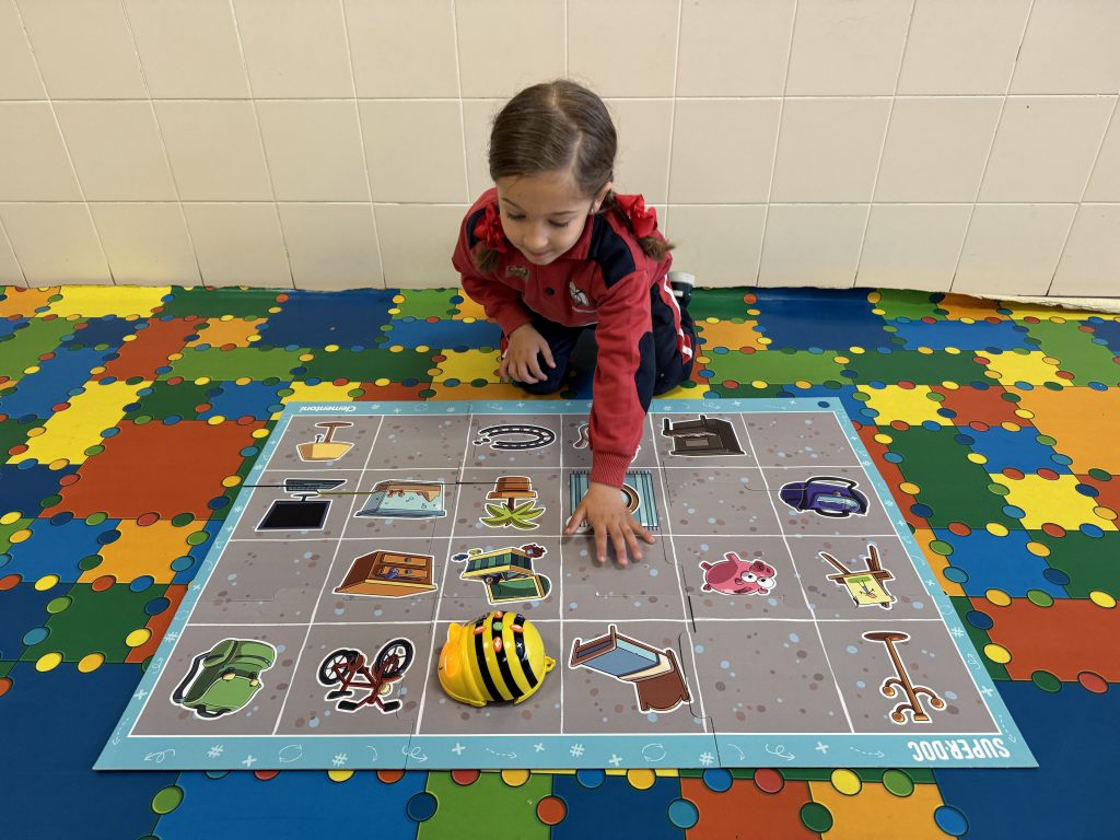 Niña de Infantil moviendo un robot de suelo sobre un tablero cuadriculado, en el aula