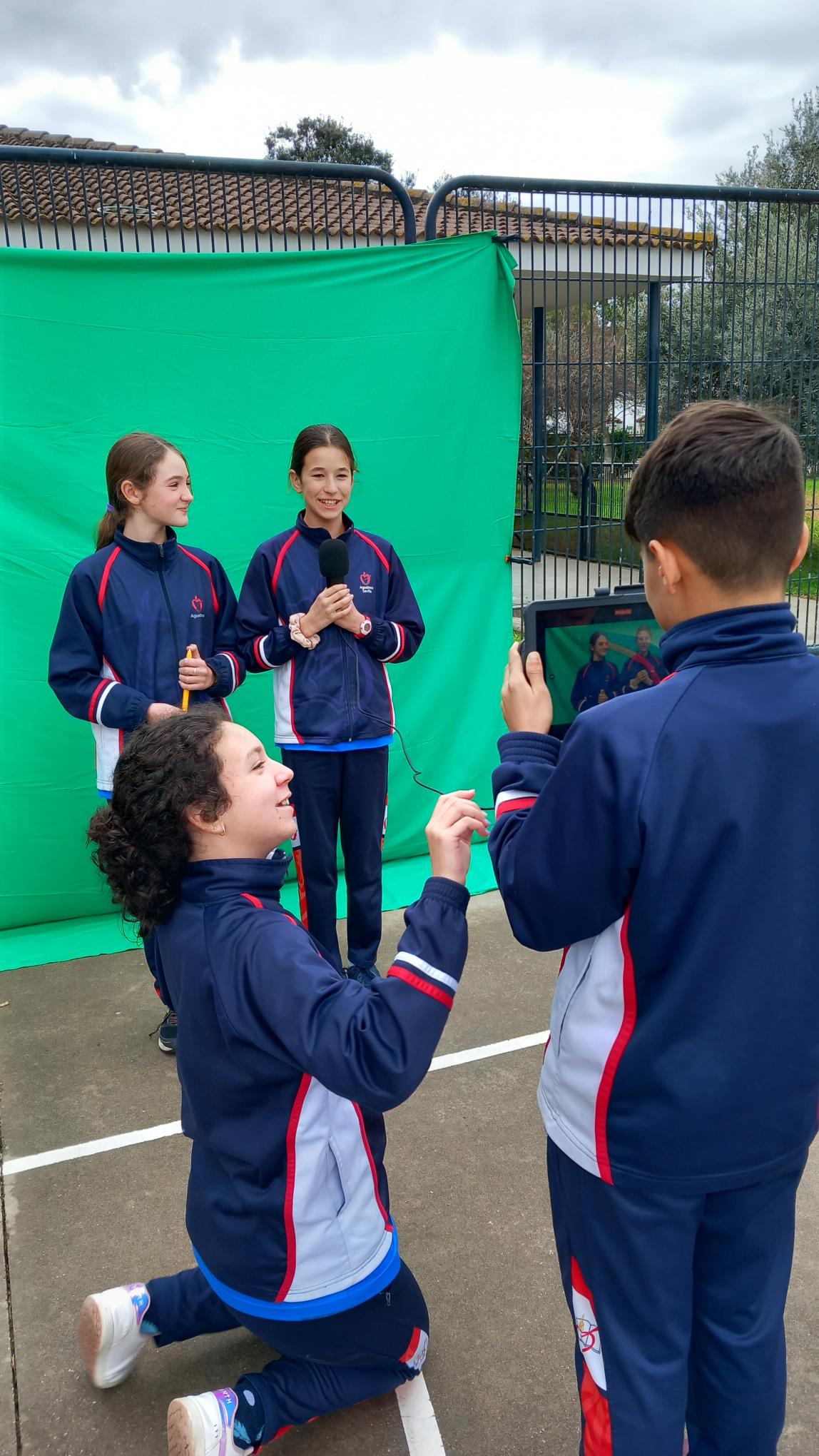 Cuatro alumnos grabando delante de una tela verde de croma, en el patio