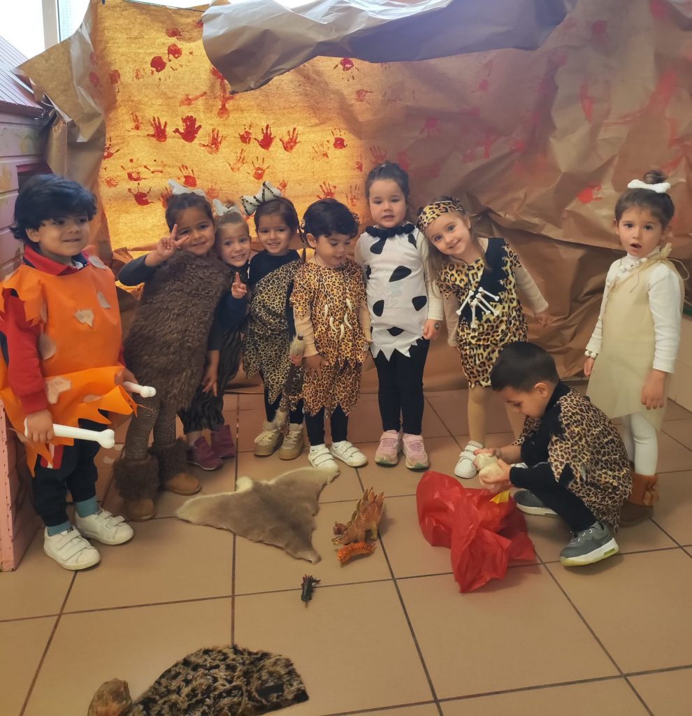 Niños de Infantil disfrazados de prehistóricos ante un decorado de cueva