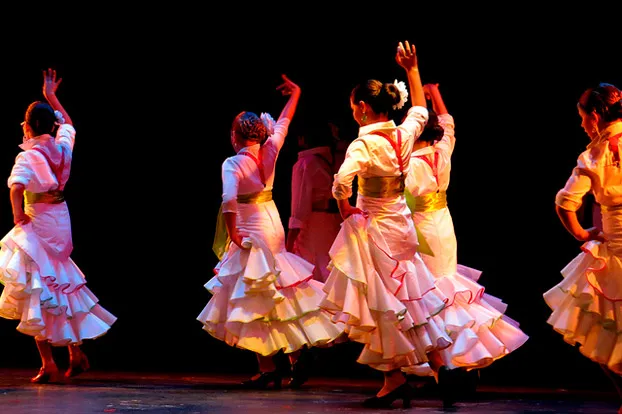 Grupo de alumnas bailando flamenco con trajes de volantes sobre el escenario