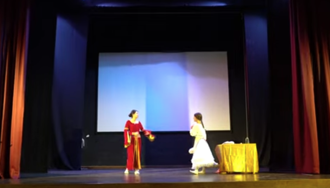 Dos alumnas representando una escena sobre el escenario del salón de actos