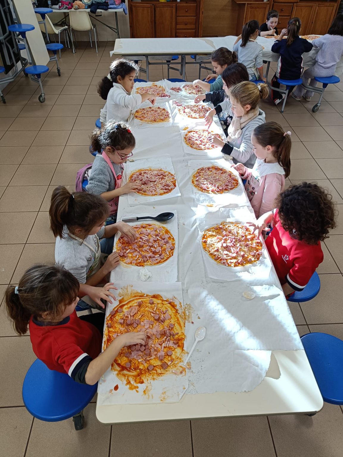 Alumnos preparando pizzas sobre una mesa larga del comedor