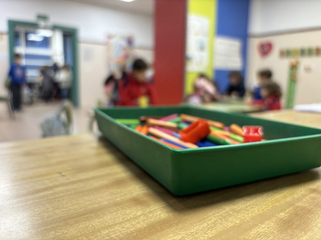 Bandeja con material de manualidades sobre una mesa del comedor, con alumnos trabajando al fondo