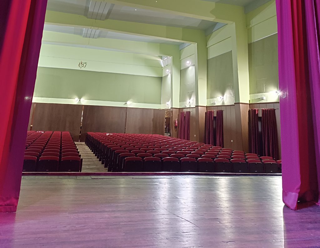Salón de actos del colegio, con el escenario en primer plano y las butacas rojas al fondo
