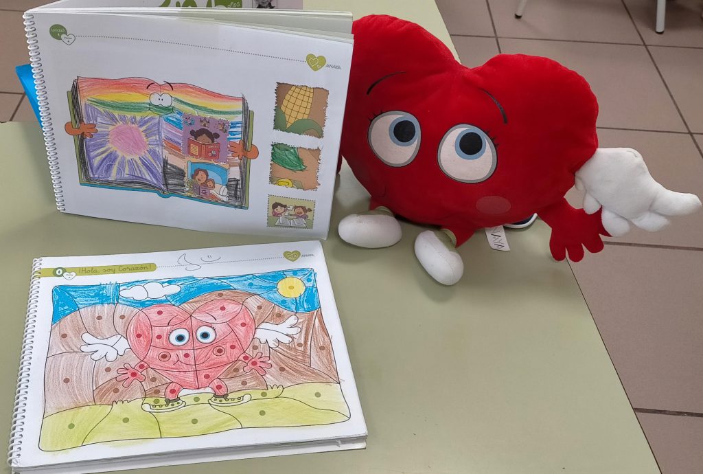 Cuaderno de trabajo abierto con dibujos, junto a un corazón de peluche