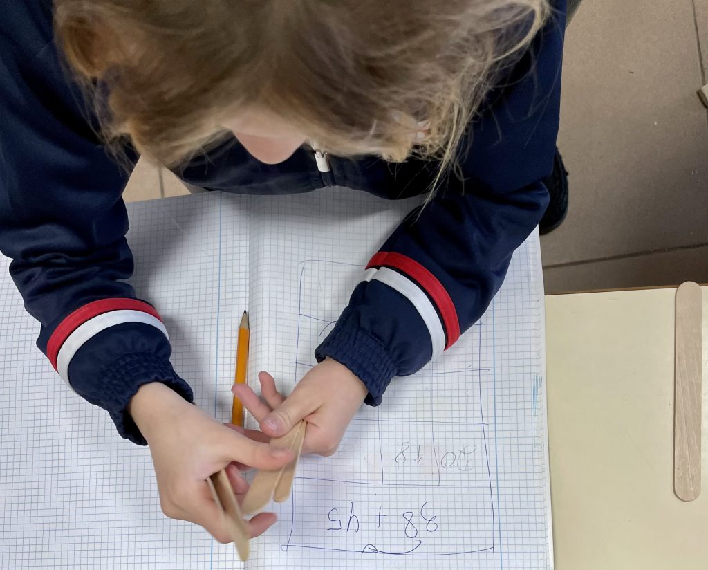 Manos de una alumna resolviendo una suma a lápiz en un cuaderno cuadriculado