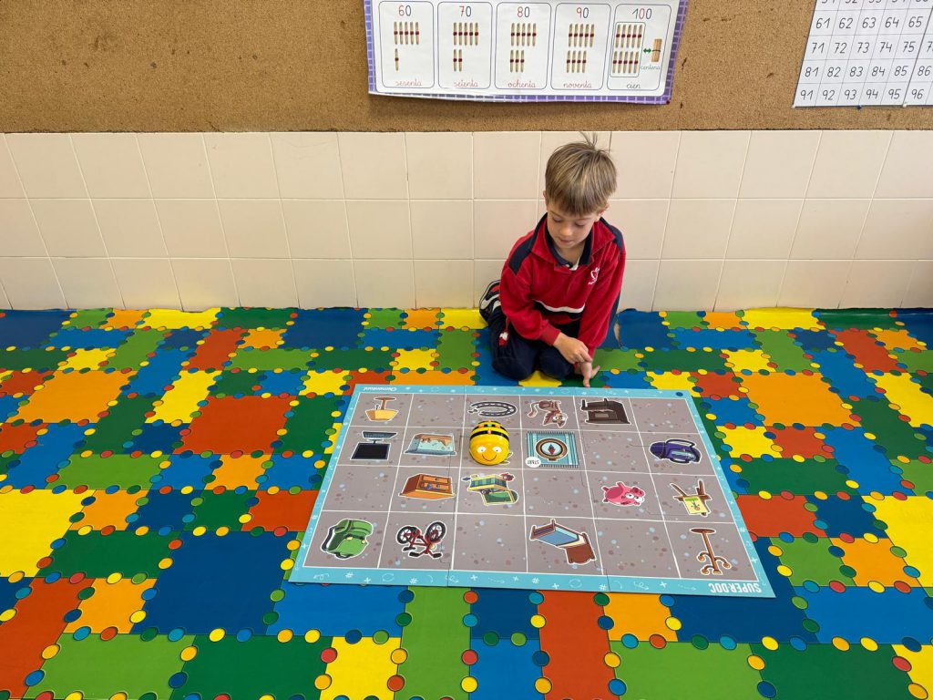 Niño de Infantil sentado junto a un tablero de programación sobre la alfombra del aula