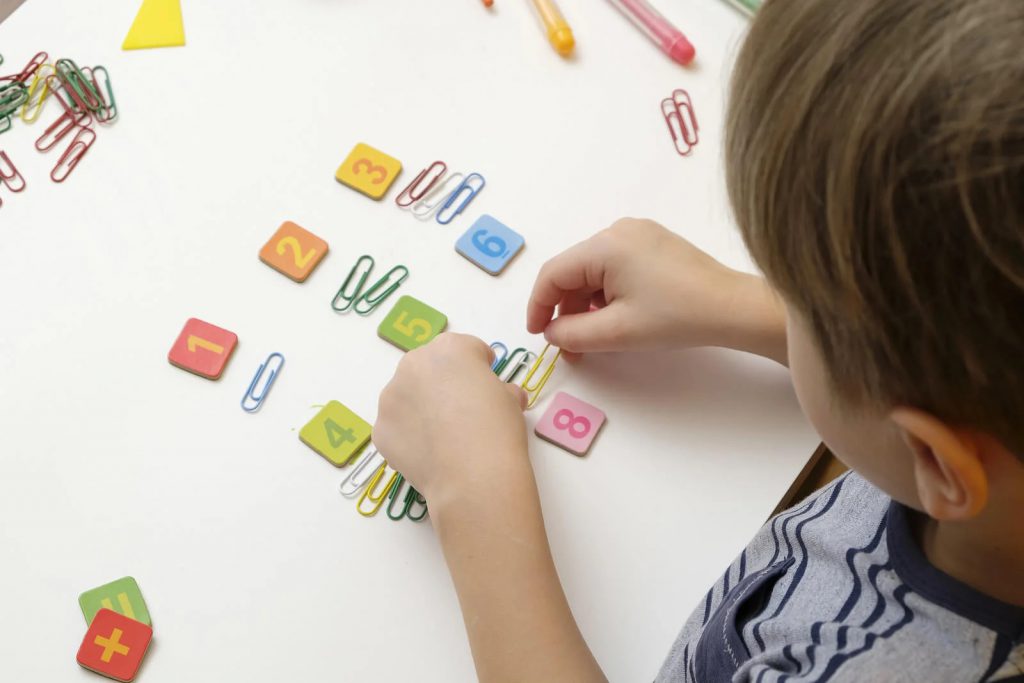 Niño colocando fichas numeradas y clips de colores sobre una mesa