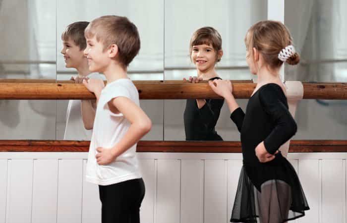 Cuatro niños y niñas en la barra de la sala de danza, frente al espejo