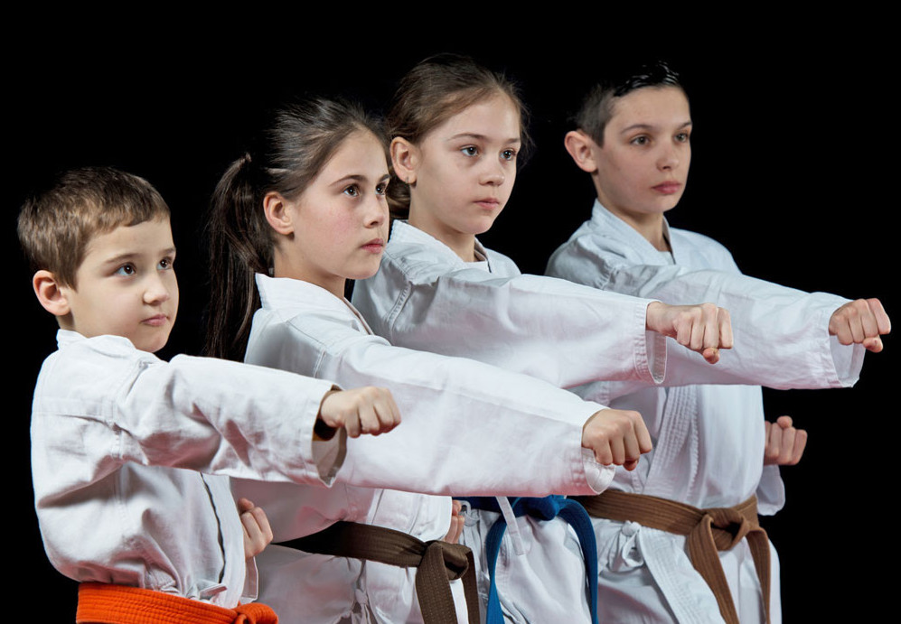 Cuatro alumnos de kárate, con kimono blanco y cinturón, ejecutando una técnica