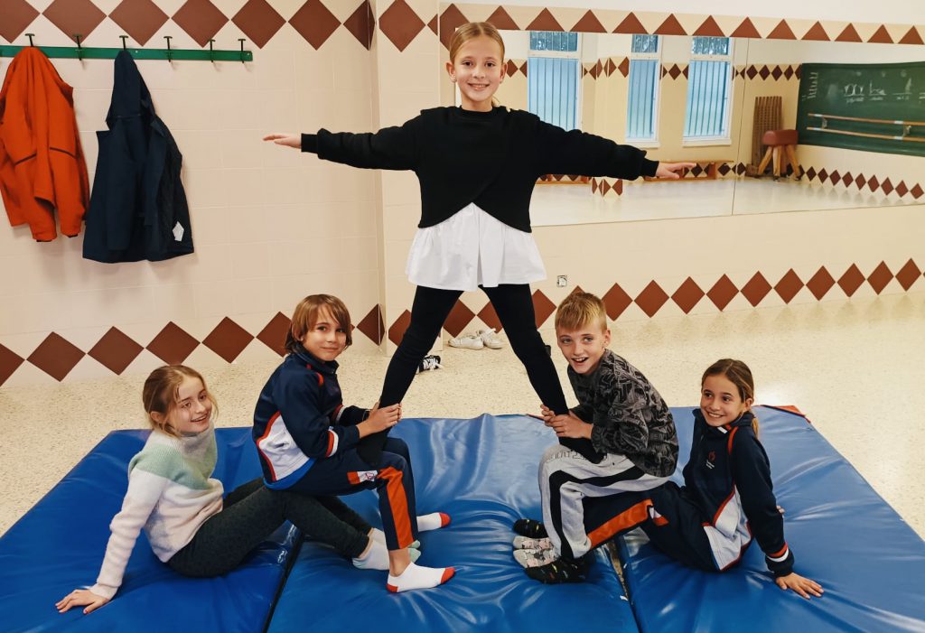 Niños y niñas haciendo una figura de acrobacia sobre una colchoneta azul