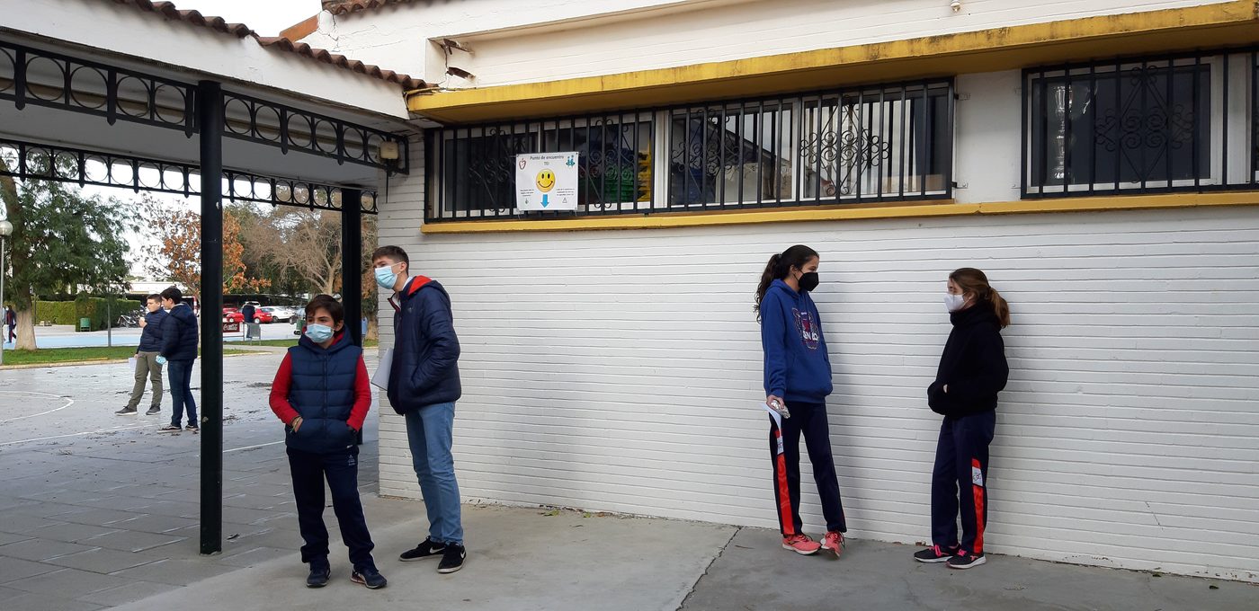 Cuatro alumnos con mascarilla apoyados en la pared del porche, separados entre sí