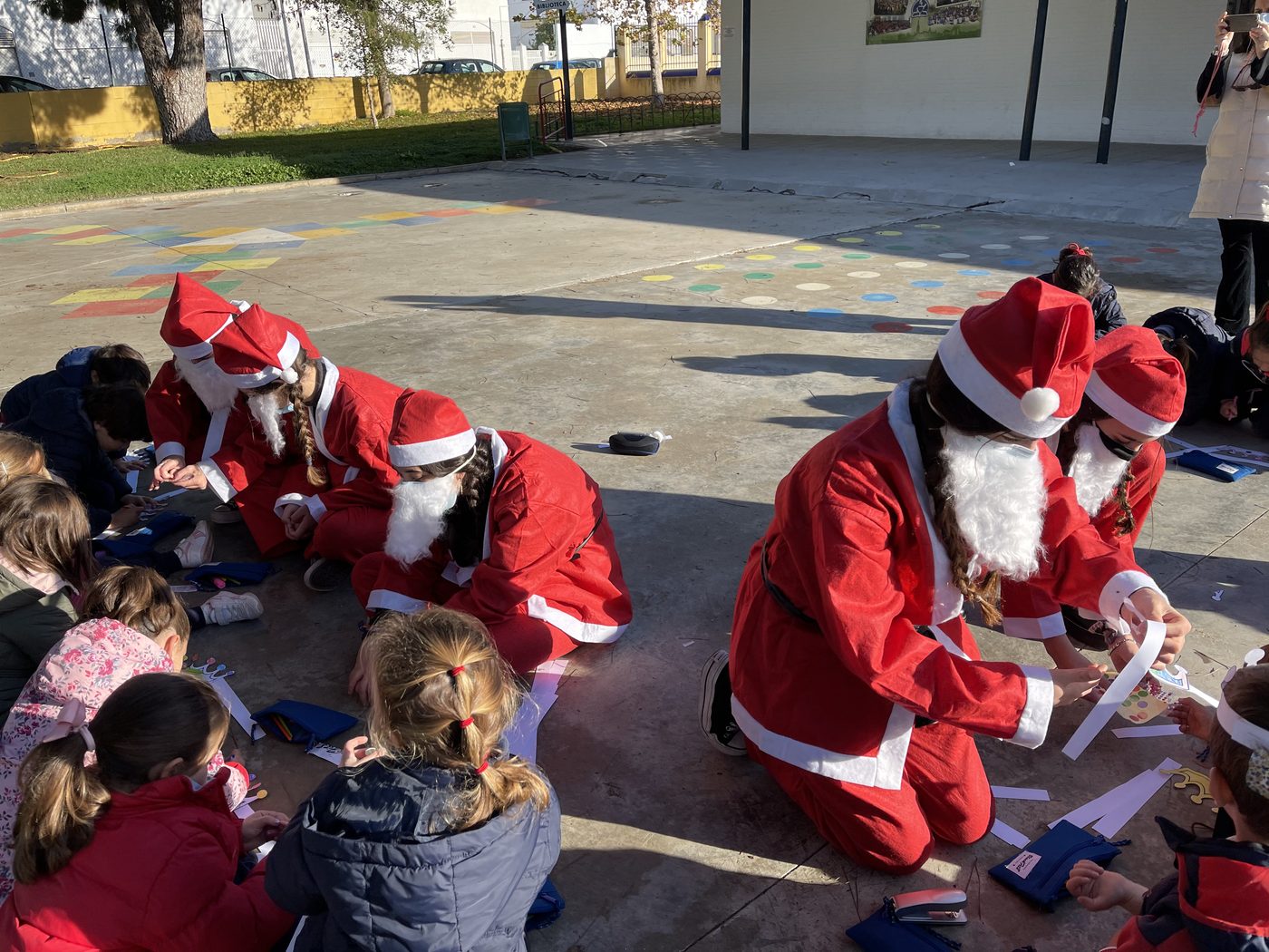 Varias personas disfrazadas de Papá Noel repartiendo regalos a niños sentados en el suelo del patio