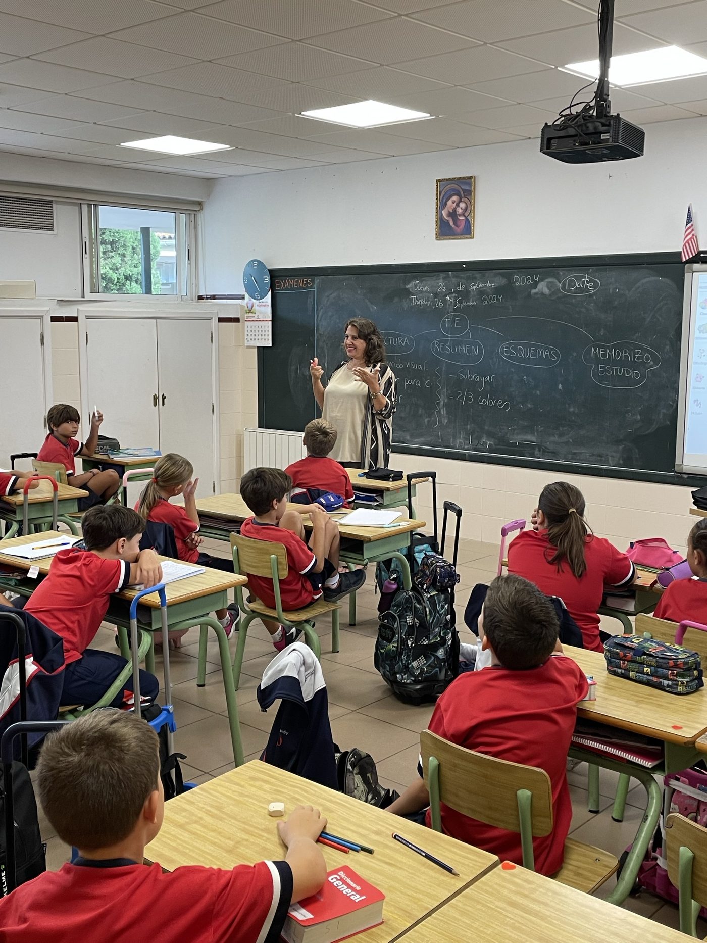 Alumnos de Primaria trabajando en sus pupitres mientras la maestra explica junto a la pizarra