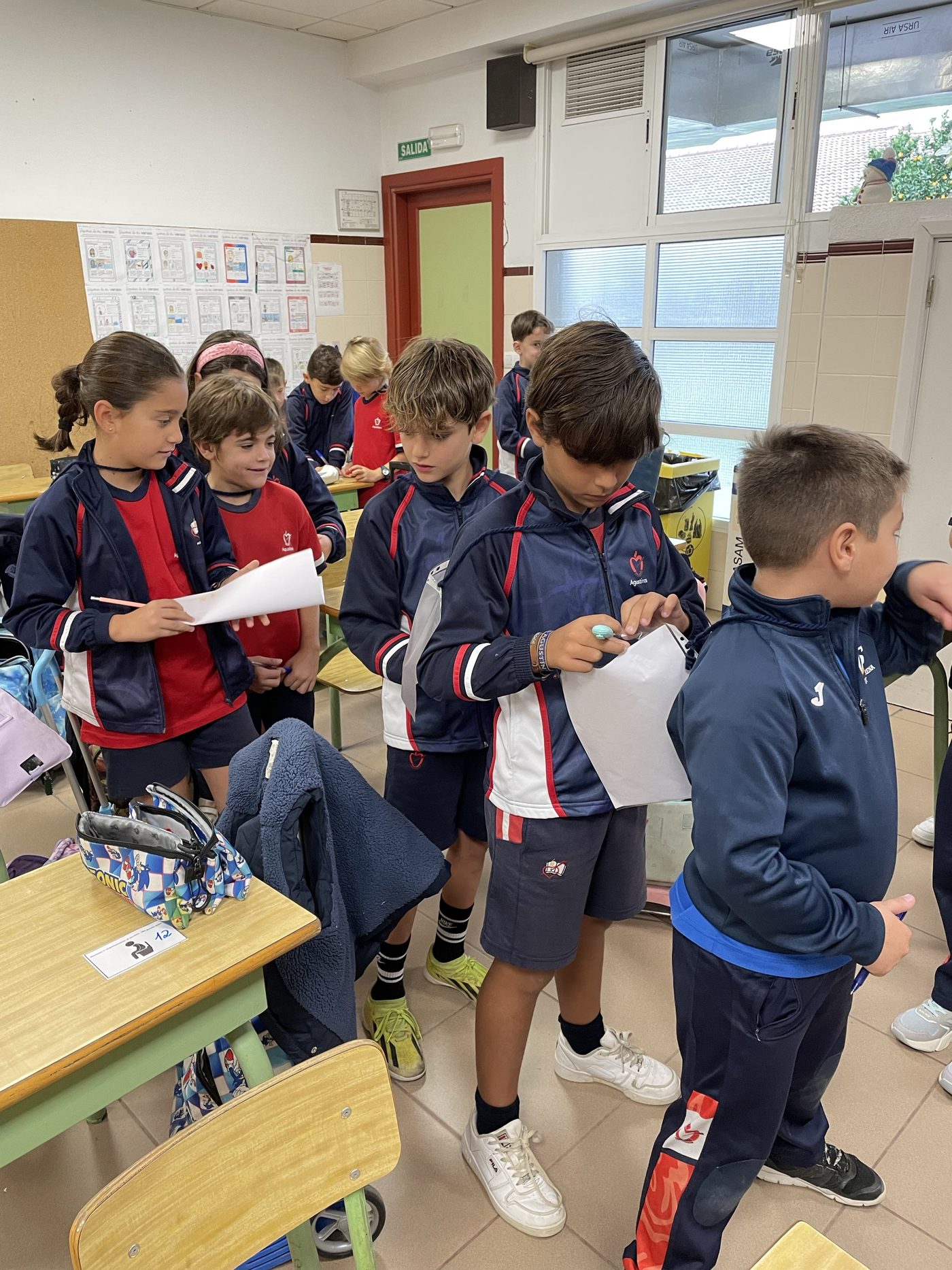 Alumnos de Primaria de pie por el aula, entrevistándose por parejas con una hoja en la mano