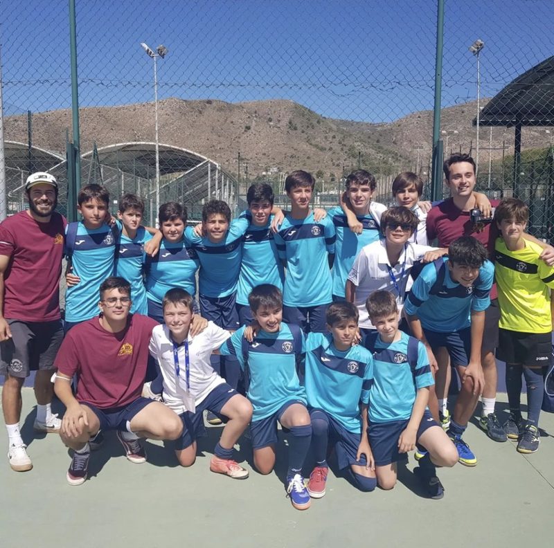 Equipo del colegio posando en una pista al aire libre, con montañas al fondo
