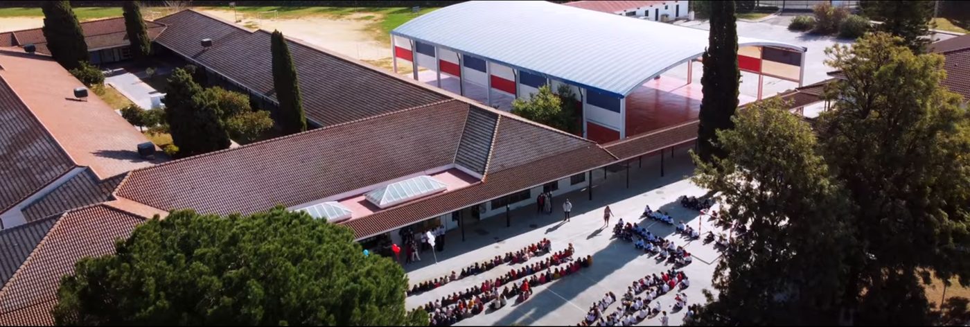 Vista aérea del colegio: los edificios de aulas, el pabellón y el patio, con cientos de personas reunidas